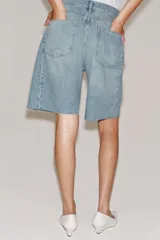 Bermuda de denim color marrón oscuro, de tiro medio y diseño relaxed fit, con cinco bolsillos, trabillas para cinto, bajo desflecado y cierre frontal con cremallera y botón.