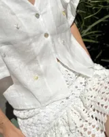 Blusa corta de lino natural color blanco, con mangas acampanadas y bordados a mano inspirados en motivos marinos como anclas, soles y estrellas de mar.