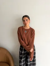 Remera de manga larga color marrón, con cuello redondo y detalle de parche cuadrado con logo bordado en el centro del pecho. Presenta un corte holgado y diseño minimalista.