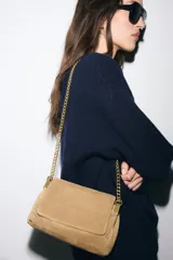 Bolso de hombro confeccionado en piel de gamuza color marrón, con diseño estructurado y pespuntes decorativos en la solapa. Cuenta con una correa de cadena metálica dorada con refuerzo de piel y cierre imantado.