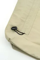 Bolso de nylon color beige, estilo tote bag, con asas de hombro, cierre superior y detalles de cordones ajustables en la parte inferior.
