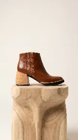 Bota corta de cuero color marrón, con diseño de paneles laterales texturizados y taco ancho de madera clara. Presenta una silueta limpia y sofisticada con suela de goma negra.