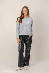 Sweater de punto gris con cuello redondo, manga larga y bolsillo frontal decorado con botones brillantes.