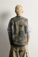 Chaleco relaxed fit de algodón con estampado de camuflaje, cuello en V, cierre frontal con cremallera y bolsillos de vivo en la cadera.