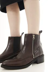 Botinetas de cuero marrón con panel elástico lateral negro y cierre metálico expuesto, con taco bajo y puntera ligeramente cuadrada.