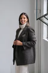 Blazer de corte sastrero en color gris oscuro con textura jaspeada. Presenta solapas clásicas, cierre frontal de doble botonadura y un bolsillo superior con detalle de pañuelo decorativo.