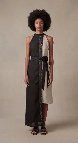 Vestido largo asimétrico, con cuello halter y corte recto. Confeccionado en dos paneles verticales contrastantes: uno negro y otro color cemento/beige claro, unidos por una tira central de encaje negro.