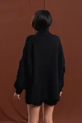 Buzo de tejido de punto grueso en color negro, con cuello alto y diseño de trenzas y relieves en toda la prenda. Presenta mangas largas con terminación ajustada y corte holgado.