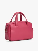 Cartera tipo bowling de Tommy Jeans, color fucsia, con doble asa superior y correa ajustable extraíble. Presenta logo metálico de la marca en la parte frontal.