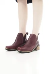 Botinetas de cuero vacuno color bordó, con diseño urbano y elegante. Presentan un detalle texturizado tipo cocodrilo en la parte trasera, taco bajo de madera y puntera cuadrada.