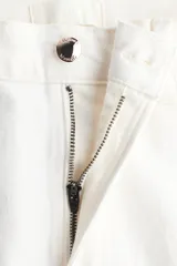 Pantalón jean de tiro alto en color blanco, con diseño de pernera recta holgada, trabillas para cinturón y cierre frontal con botón metálico. Presenta pliegues marcados al frente y bolsillos laterales.