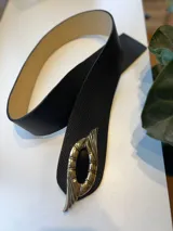 Cinto negro de cuero con hebilla metálica con diseño abstracto.