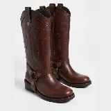Bota de caña alta estilo western en cuero color marrón, con detalle de arnés con tachas metálicas y tiradores laterales.