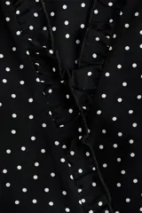 Vestido corto negro con estampado de lunares blancos, escote en V con volados, mangas largas abullonadas y cordón ajustable en la cintura.