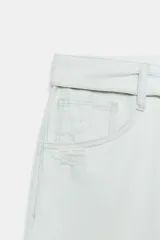 Bermuda tipo jorts de denim en color celeste claro, con tiro medio, diseño de cinco bolsillos y cinturilla doblada. Presenta roturas decorativas en la parte delantera y cierre frontal con cremallera y botón metálico.