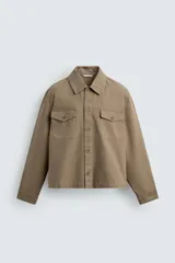 Sobrecamisa de corte boxy fit confeccionada en algodón con estructura canvas y efecto lavado. Presenta cuello solapa, cierre frontal con botones, mangas largas con puños abotonados y bolsillos de plastrón con solapa en el pecho. Incluye detalles bordados a tono en las mangas.