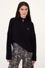 Sweater de punto acanalado con cuello alto y cierre frontal parcial. Presenta un diseño tricolor en bloques con cuerpo color crema, cuello y puños azul marino, y detalles en rojo en las mangas. Incluye una pequeña etiqueta con logo en el pecho.