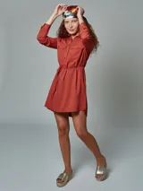 Vestido camisero color verde óxido, con cuello camisero, mangas largas con puños abotonados, dos bolsillos con solapa en el pecho, cinturón de lazo y cierre frontal con botones.