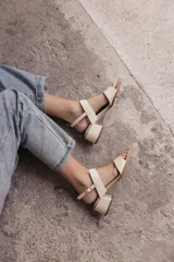 Sandalia de cuero color beige claro (off white) con taco ancho y tiras finas ajustables con hebilla metálica dorada en el tobillo.