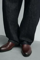 Bota estilo chelsea de cuero color marrón, con paneles elásticos laterales, tirador trasero y horma en punta con suela de tacón bajo.