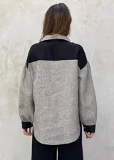 Camisa a rayas verticales grises y blancas, de lino, con cuello clásico, cierre frontal con botones, mangas abullonadas 3/4 con puños elásticos negros y corte holgado.