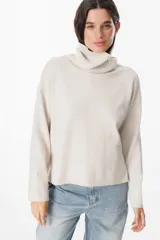 Sweater de punto color beige con cuello alto tipo polera, de corte holgado y mangas largas con puños acanalados.
