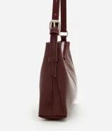 Cartera tipo baguette de tamaño pequeño en cuero sintético color bordó, con correa ajustable y cierre de cremallera metálica con herrajes en níquel.