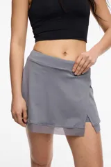 Falda short deportiva color violeta, con calza interna y bolsillo lateral. Presenta un frente cruzado y detalle de microtul en el dobladillo.