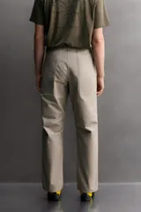 Pantalón de corte tapered fit color beige, confeccionado en tejido ligero de algodón con estructura rip stop. Cuenta con bolsillos de plastrón delanteros con acceso curvado, pinzas en las rodillas para mayor movilidad, y cierre frontal con cremallera y botón a presión.