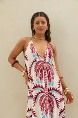 Vestido largo de diseño holgado, con estampado de palmeras en tonos bordó y celeste sobre base cruda. Presenta escote halter profundo y tirantes finos que se atan al cuello.