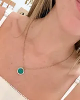 Collar de cadena fina dorada con dije circular que presenta una base de resina verde rodeada por una hilera de strass brillante.