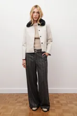 Chaqueta corta color beige con cuello de piel sintética negra, cierre frontal de botones y bolsillos laterales.