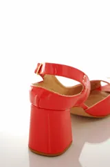 Sandalias de cuero charol color coral con taco mediano forrado, diseño open toe y tira ajustable en el talón. Presenta un aplique decorativo desmontable en forma de corazón blanco en la parte delantera.