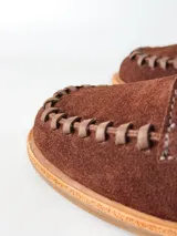 Sandalias de cuero gamuzado color marrón chocolate, diseño tipo huarache con tiras entrelazadas, tira en el empeine, talón cerrado y hebilla metálica de ajuste lateral.