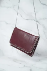 Cartera de hombro con solapa y bordes ribeteados con una cadena metálica entrelazada. Presenta un diseño tipo sobre con acabado texturizado y una correa de cadena larga.