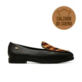 Zapato tipo mocasín de cuero negro con detalle de capellada en pelo con estampado animal print. Presenta puntera redonda, taco bajo y logo metálico dorado en el lateral.