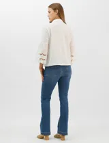 Camisa blanca de corte recto con cuello camisero y cierre frontal de botones. Presenta mangas tres cuartos acampanadas con detalles de bordado suizo calado en los puños y en el ruedo inferior.