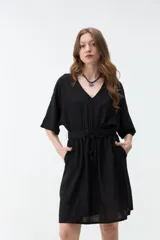 Vestido corto negro con escote en V, mangas cortas amplias, cintura elasticada con cordón ajustable para lazo y bolsillos laterales.