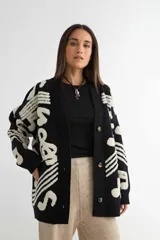 Saco tipo cardigan de punto, color negro con diseño de notas musicales y compases en color crema. Presenta cierre frontal con botones, cuello en V y puños acanalados.