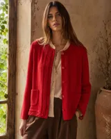 Cárdigan tejido en lana merino color rojo, con cuello redondo, bolsillos frontales aplicados, detalles de textura en los bordes y cierre frontal con botones.