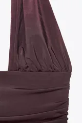 Body color borgoña de cuello halter con escote pronunciado, detalle de pieza metálica y aplicación joya. Tejido drapeado y cierre inferior con botones a presión y en cuello con gancho metálico.