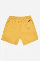 Short de baño color mostaza, de tela ligera y secado rápido, con cintura elástica y cordón de ajuste blanco. Posee bolsillos laterales y uno trasero, y un pequeño logo de goma en la parte inferior derecha.