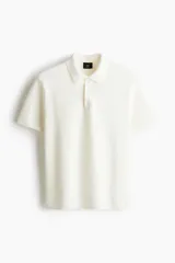 Remera polo de manga corta confeccionada en punto texturizado suave, con cuello clásico y tapeta de botones. Presenta un corte estándar y remates acanalados en puños y bajo.