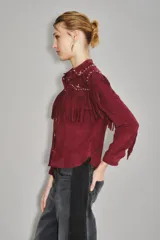 Camisa estilo western color bordó, confeccionada en gamuza caprina, con flecos largos en el canesú delantero y en las mangas. Presenta cuello con tachas metálicas plateadas.