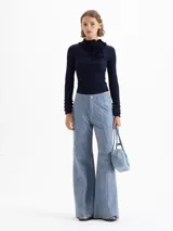 Sweater de tejido de punto fino color marrón, con ajuste al cuerpo, cuello alto con detalle de volados y moño, y mangas largas con puños acampanados con volados.