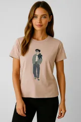 Remera de algodón color beige con estampado de una figura femenina con lentes, chaqueta verde, pantalón a rayas y un pañuelo azul. El estampado incluye lentejuelas.