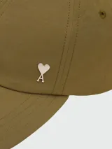 Gorra de béisbol color verde oliva, confeccionada en nylon, con visera curva y un pequeño pin metálico con el logo de corazón de Ami Paris en el frente.