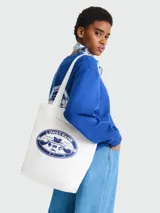 Bolso tipo tote de color marfil de la colaboración Longchamp x Constantin, con diseño de asa larga para hombro. Presenta un estampado gráfico ovalado en color azul en el frente con el logo de la marca y motivos ilustrados.