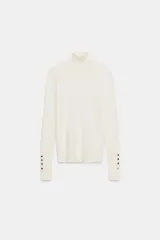 Jersey de punto liso en color beige, con cuello alto y manga larga con detalle de botones metálicos en los puños.