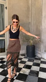 Falda tejida a mano en crochet, con diseño a rayas horizontales en tonos marrón y negro con hilos de lurex dorado. El ruedo presenta una cascada de flecos largos y finos en color negro.